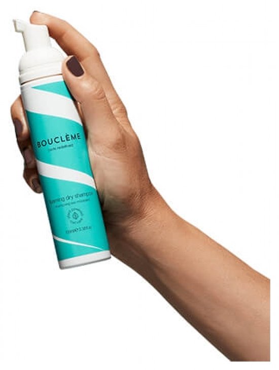 Hand houdt een fles met teal- en witte spiraalvormige strepen voor droogshampoo vast.