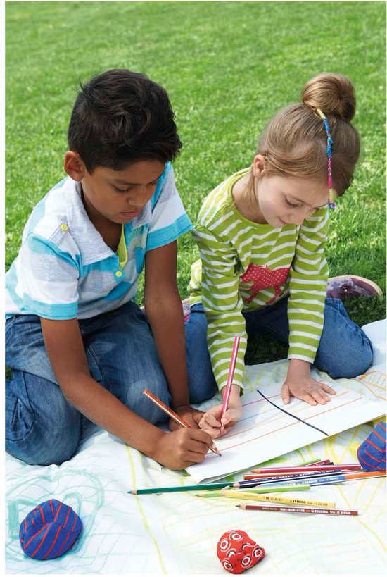 Twee kinderen, jongen en meisje, zitten op een kleed in het gras en tekenen. Veel kleurpotloden liggen naast hen.