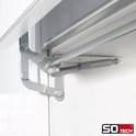 Detail van een metalen scharnier en gasdrukveer aan de binnenkant van een witte kastdeur.