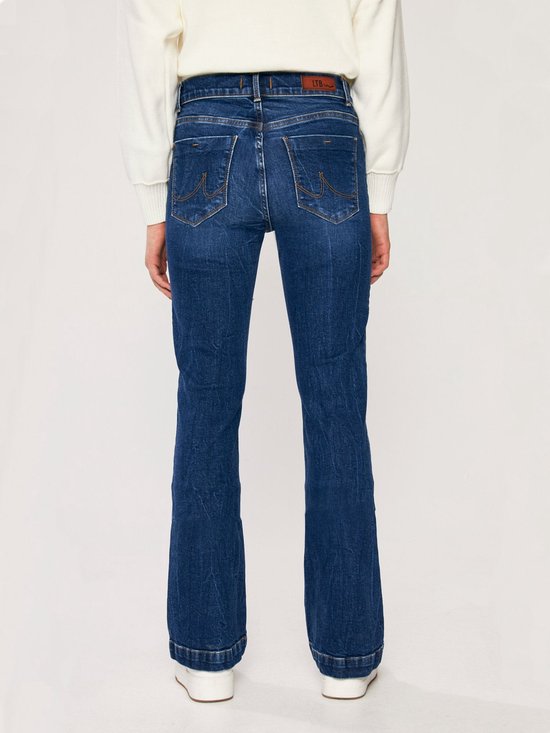Achterkant van een vrouw in een donkerblauwe flared jeans met een omgeslagen zoom.