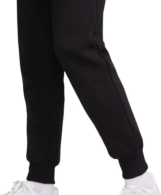Onderkant van zwarte joggingbroek met witte sneakers en witte sokken.