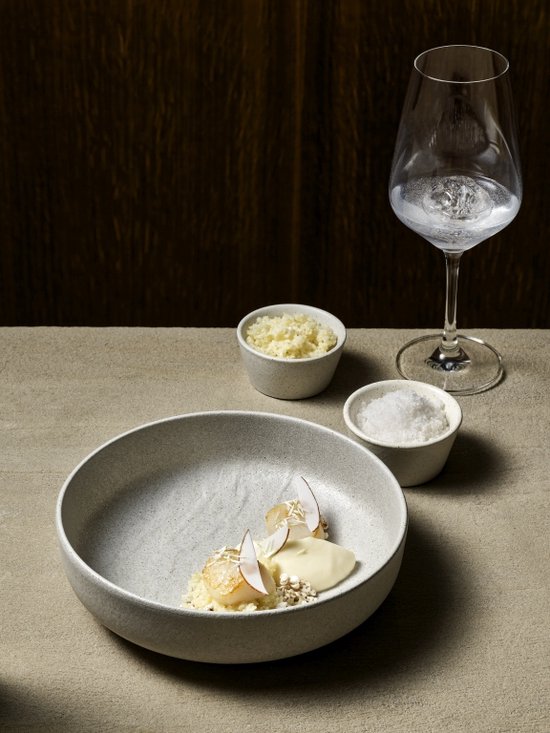 Elegant wijnglas gevuld met water op een tafel naast een kom met eten en kleine bakjes met ingrediënten.