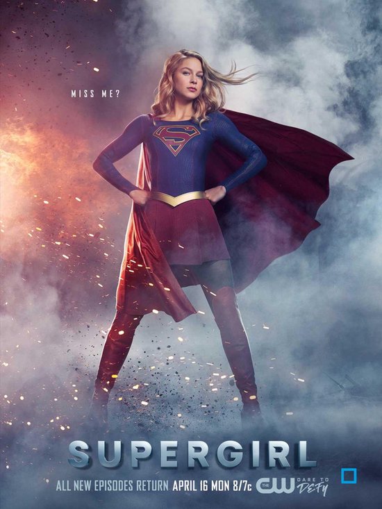 Supergirl in blauw pak met rood masker en cape, staat poseerend met handen in de zij.