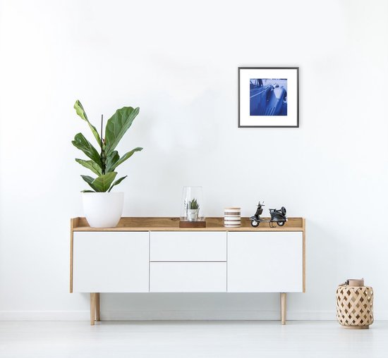 Zwarte fotolijst met blauwe print van een auto, staand op een kast met plant.