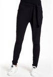 Een vrouw in een zwarte broek met strikceintuur en witte sneakers.