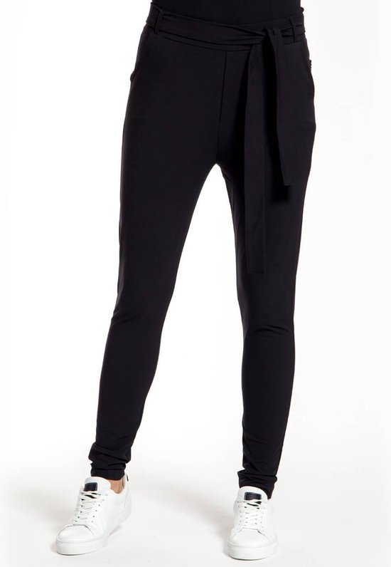 Een vrouw in een zwarte broek met strikceintuur en witte sneakers.