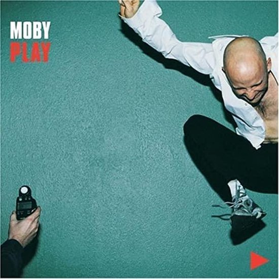 Moby Play albumhoes met Moby die in de lucht springt, in een witte blouse en zwarte broek.