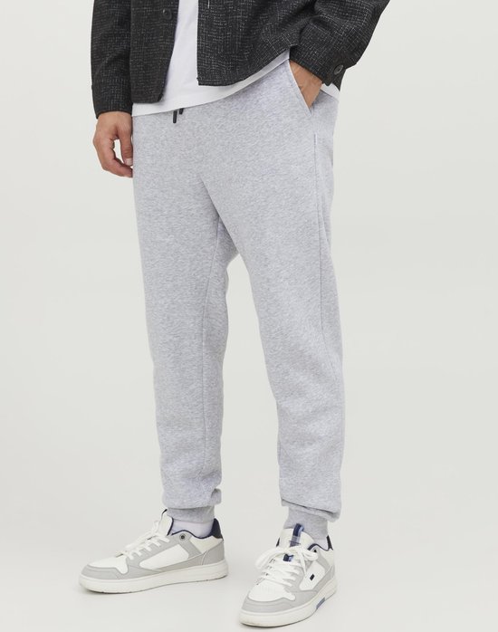 Man met lichtgrijze joggingbroek en sneakers, gedragen met een donkere jas.