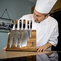 Een kok bekijkt een houten messenblok met zes Japanse messen met damastpatroon en unieke handvatten.