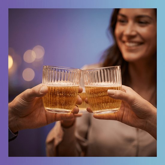 Un groupe de personnes trinque avec des verres à côtes verticales. Ambiance festive avec des lumières bokeh.