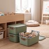 Groene opbergboxen met bruine handgrepen, één gevuld met speelgoed zoals een olifantje, houten regenboog en autootjes.
