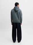 Achterkant van een man in een effen, donkergroene hoodie en zwarte broek.