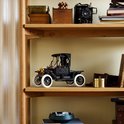 Zwarte LEGO Ford Model T op een houten plank naast decoratieve objecten zoals een oude camera.