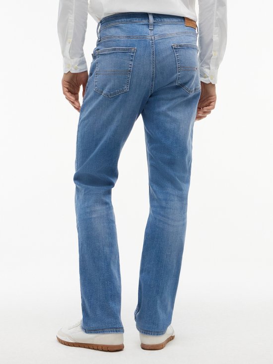 Achterkant van een man in een lichte spijkerbroek met witte top en witte sneakers.