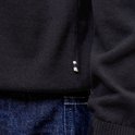 Detail van een zwart gebreid poloshirt met kleine rode en witte labeltjes op de zoom.