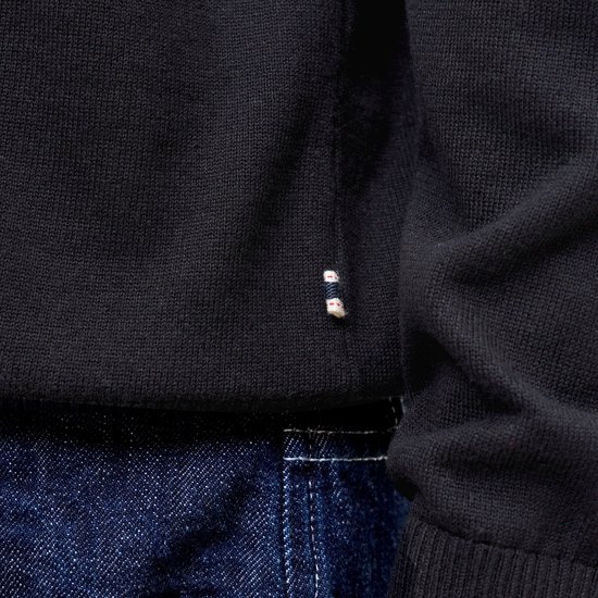Detail van een zwart gebreid poloshirt met kleine rode en witte labeltjes op de zoom.