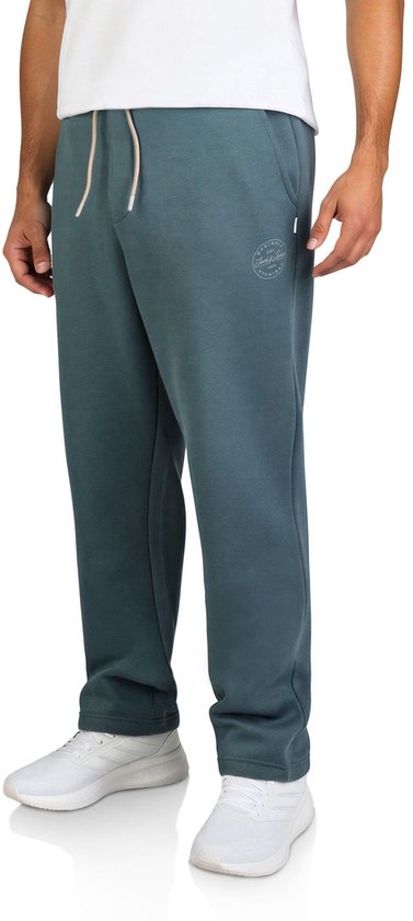 Zijaanzicht van een blauwgroene joggingbroek met ronde Jack & Jones Originals-opdruk, trekkoord en witte sneakers.