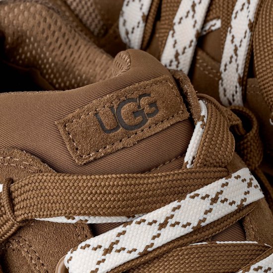 Close-up van de tong van een bruine UGG-sneaker met het UGG-logo op een suède patch en gedetailleerde veters.