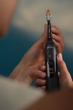 Zwarte Philips Sonicare tandenborstel in handen met schermmelding: REPLACE BRUSH HEAD.