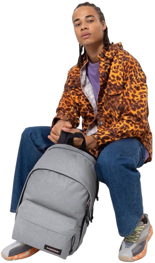 Jongeman met een grijze Eastpak rugzak met een luipaardprint jasje, paars shirt en spijkerbroek.