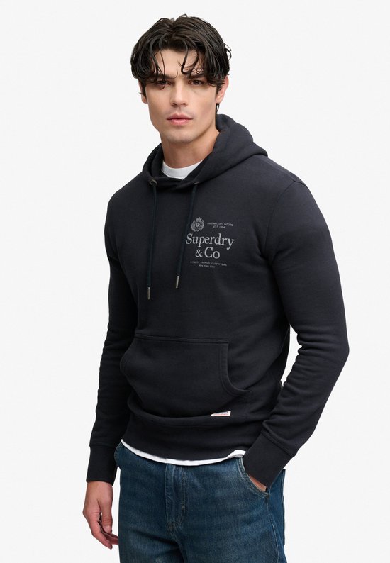 Model draagt donkerblauwe hoodie met witte onderlaag en spijkerbroek.