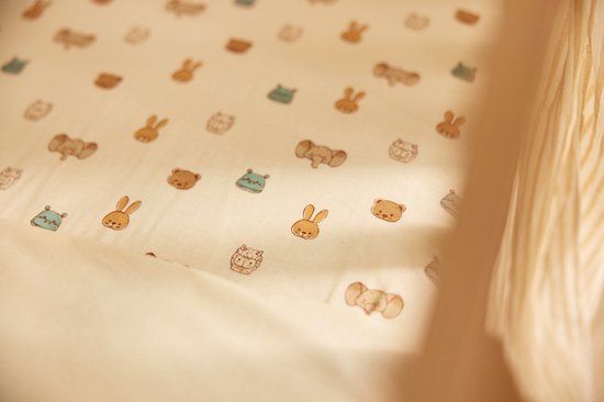 Detail van een wit hoeslaken met een print van beige en blauwe dierenkoppen: beer, konijn, olifant, nijlpaard.