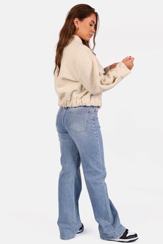 Model in licht beige teddy bomberjack met drukknoopsluiting en jeans.