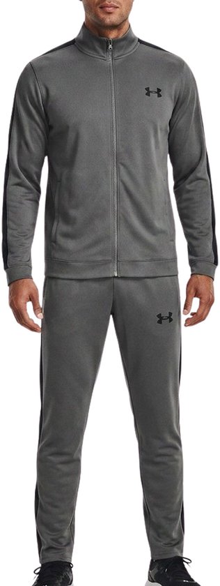 Man met grijze trainingsset: jack met zwarte strepen en logo, en broek met zwarte strepen en logo.