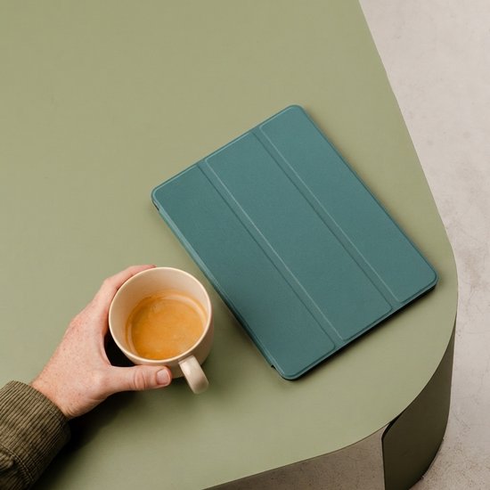 Étui pour tablette vert foncé sur une table vert olive, à côté d'une tasse de café.