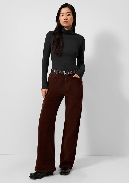 Model in zwarte coltrui met lange mouwen en bruine ribfluwelen broek met riem.