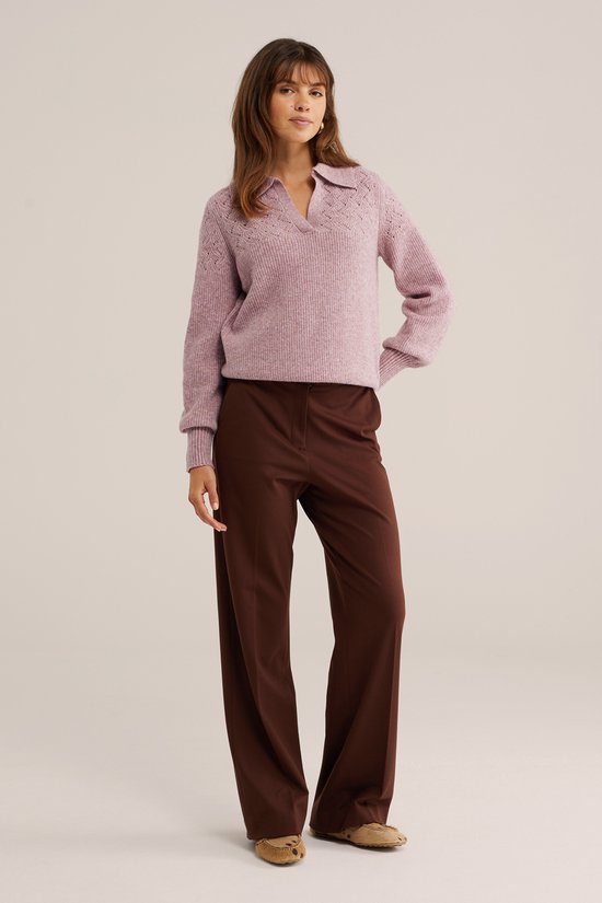 Model in lichtroze trui met polokraag en bruine pantalon.