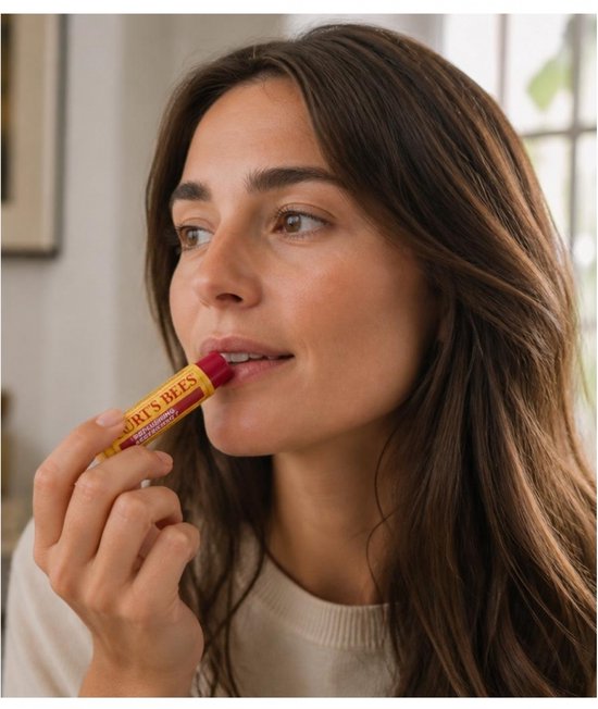 Vrouw met bruin haar brengt Burt's Bees lippenbalsem met granaatappel aan.