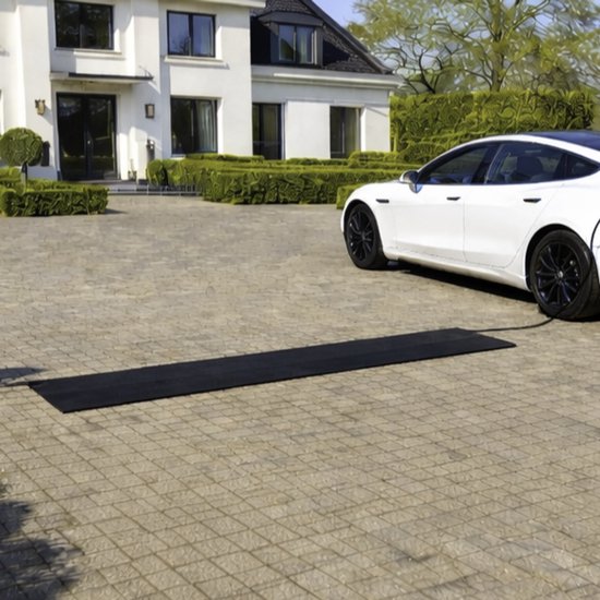 Zwarte kabelmat met ribbelstructuur op een betegelde oprit, naast een witte elektrische auto.