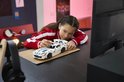 Een meisje met een rode jas legt een witte LEGO Technic Dodge Viper GTS-R sportauto met blauwe strepen op een bureau.