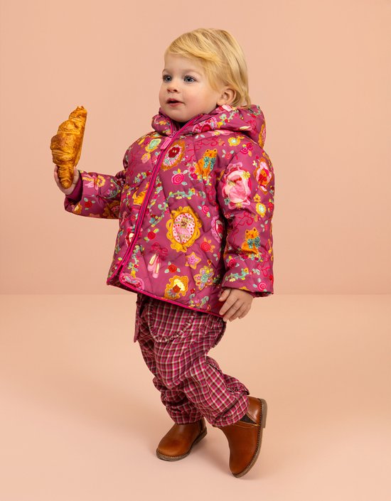Meisje met blond haar met een croissant in een roze jas met veelkleurige print.