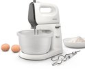 Een witte Philips handmixer met grijze bovenkant, gemonteerd op een draaiende witte kom, naast twee eieren en bloem.