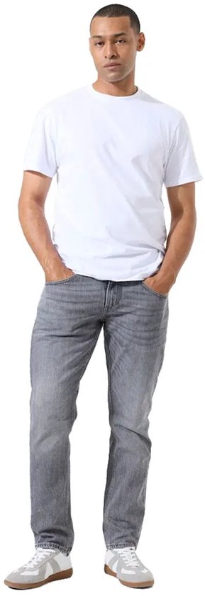 Man in witte T-shirt en grijze slim fit jeans, handen in de zakken.