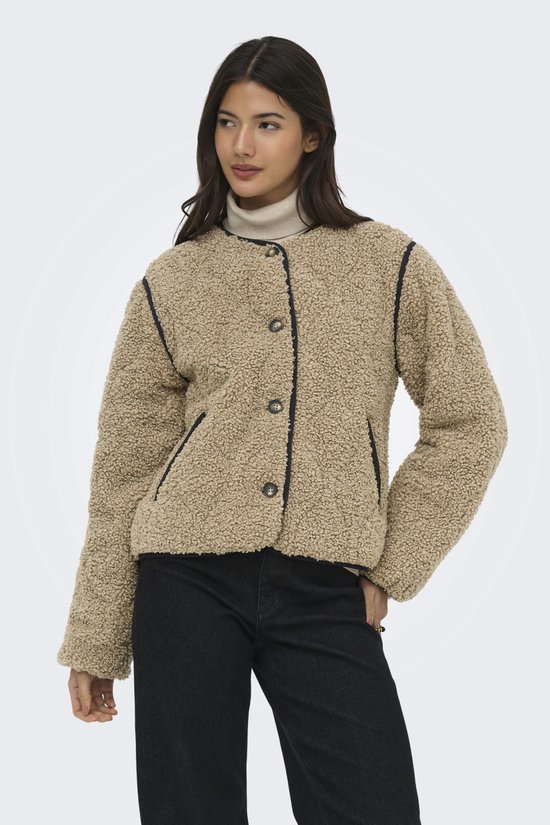 Model draagt een bruine teddy jas met zwarte biezen en knopen, gecombineerd met een coltrui en jeans.