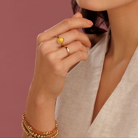 Gouden ring met een ovale, oranje citrien edelsteen gedragen op een hand met bijpassende armband.