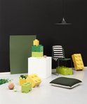 Minimalistische kamer met groene en gele Lego opbergdozen, een witte kubus, een stoel en losse Lego-blokjes.