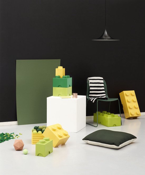 Minimalistische kamer met groene en gele Lego opbergdozen, een witte kubus, een stoel en losse Lego-blokjes.