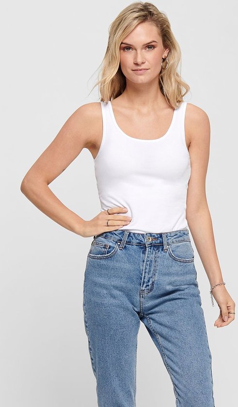 Model met een witte mouwloze top, gecombineerd met een spijkerbroek.