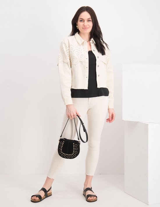 Model in een lichte, skinny jeans met rafels, wit jasje met kanten details en zwarte tas.