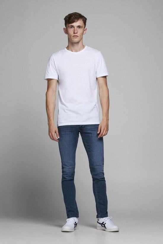 Man in spijkerbroek en wit t-shirt, staand.