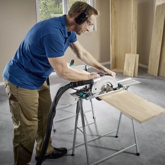 Man met blauwe polo en beige werkbroek zaagt een houten plank met een cirkelzaag op een geleiderail.