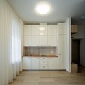 Een ronde, witte plafondlamp verlicht een moderne keuken met witte kasten en een houten aanrecht.