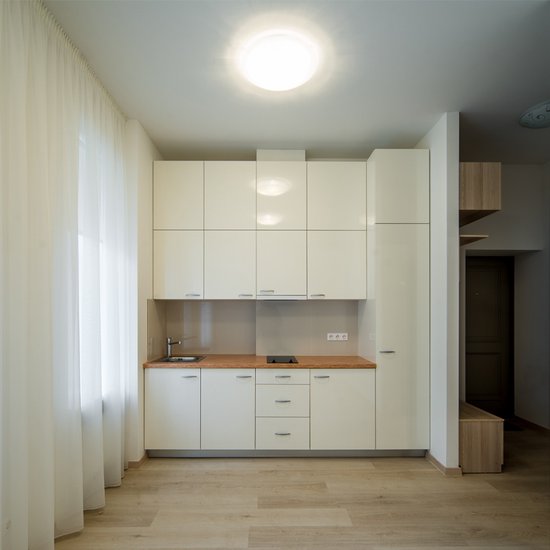 Een ronde, witte plafondlamp verlicht een moderne keuken met witte kasten en een houten aanrecht.