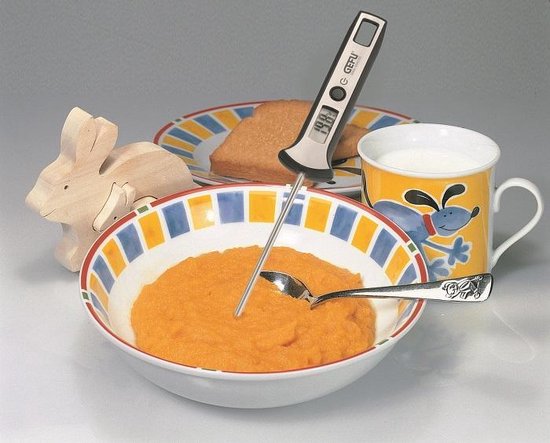 Kom met oranje puree, een mok melk, toast en een houten konijn, met thermometer.