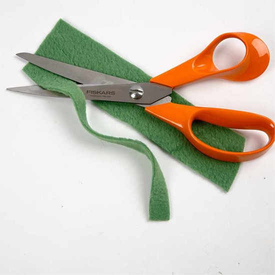 Oranje Fiskars schaar knipt door groen vilt.