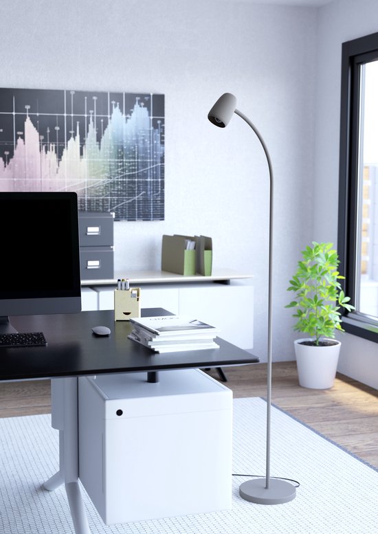 Grijze staande lamp met gebogen arm en verstelbare lampenkap, naast een bureau met monitor.